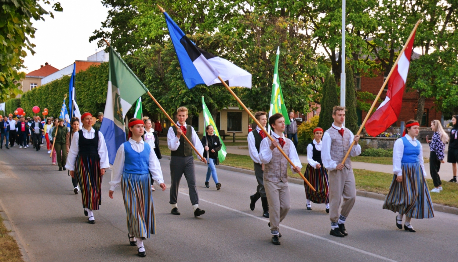 Jaunieši tautas tērpos gājienā ar latviešu un igauņu karogiem