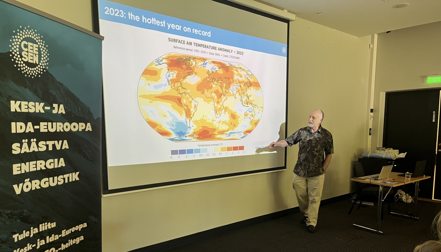 Vīrietis runā pie pasaules kartes ar gaisa temperatūras anomālijām 2023. gadā 