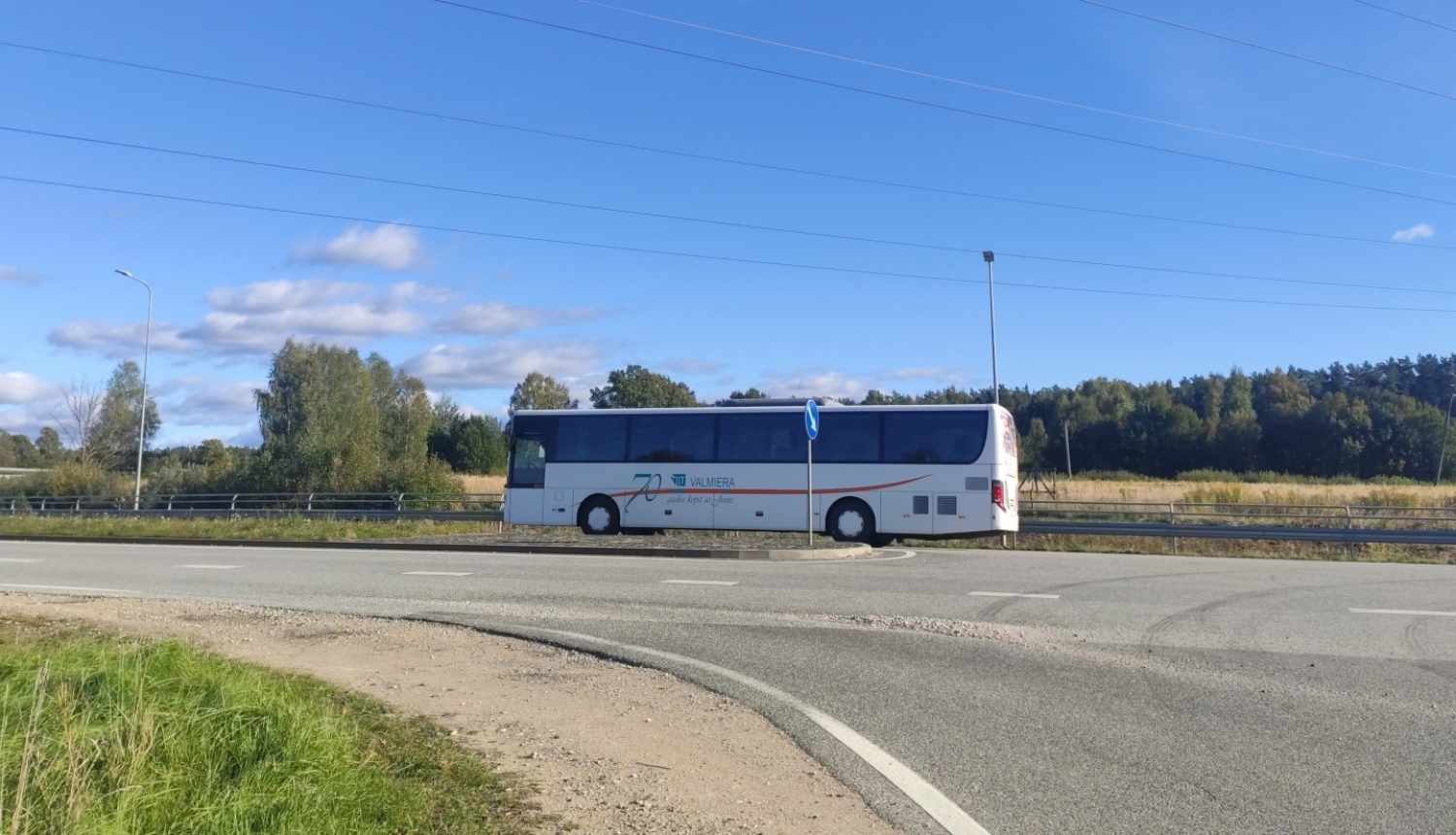 Balts autobuss uz ceļa, fonā zilas debesis